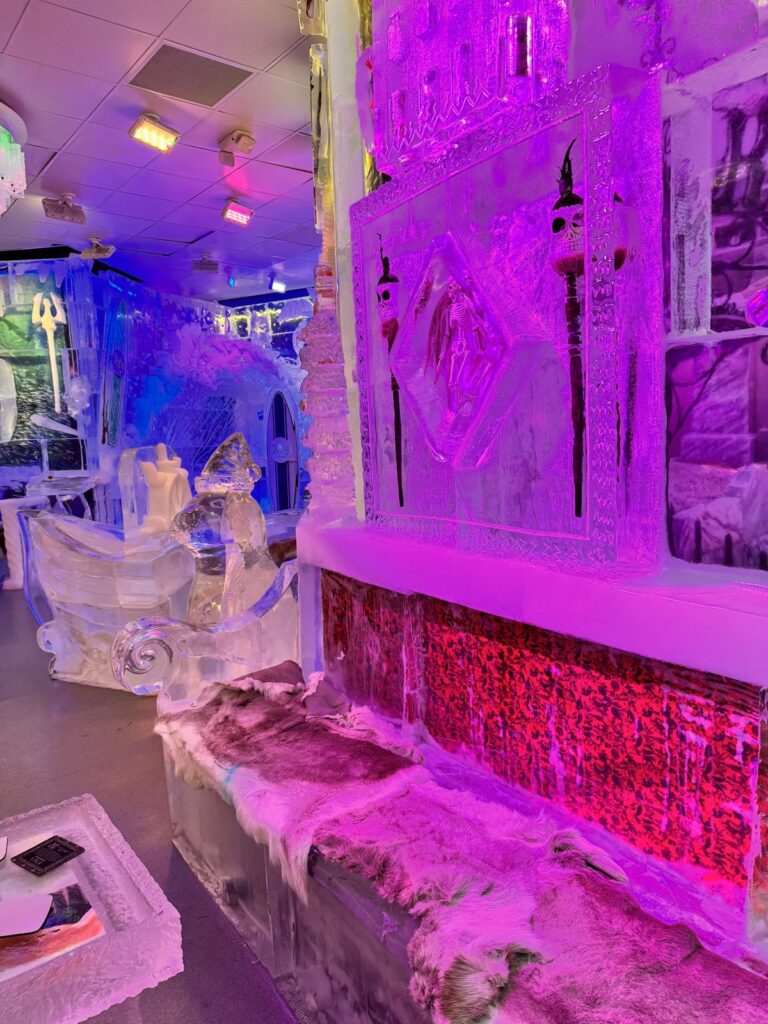 Carved ice walls and fur-covered ice benches lit in pink and purple at an ice bar at The Venetian
