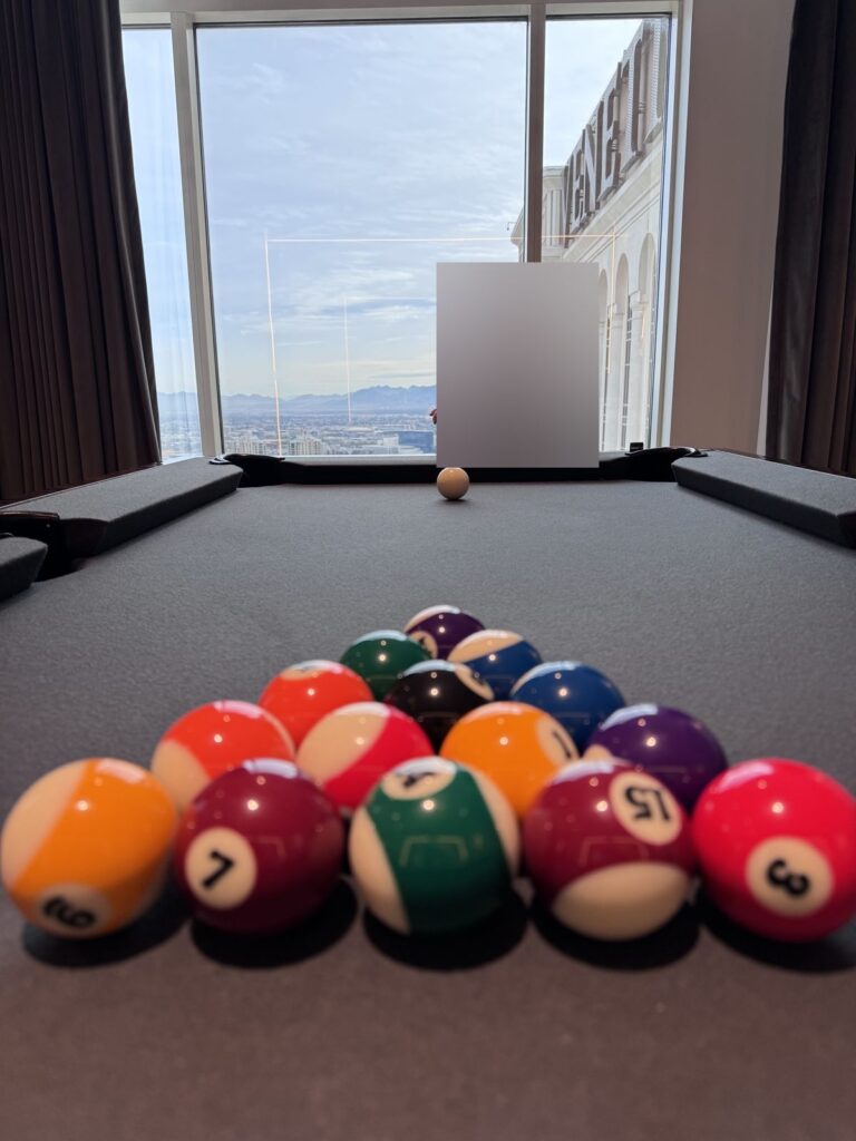 Child lining up a shot at the pool table in a Venetian suite with a view of the Strip